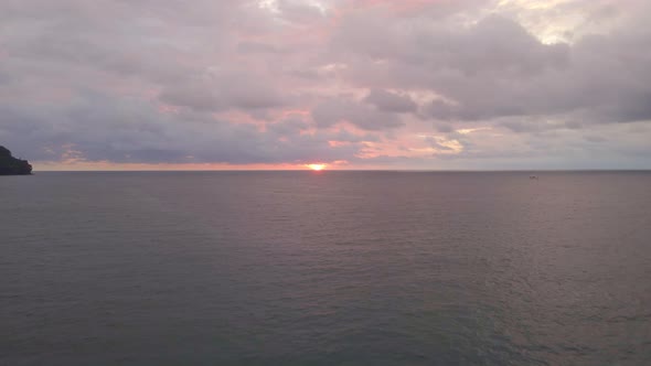 The orange sun glimpsing between heavy evening clouds and the warm waters of the south pacific. Wide