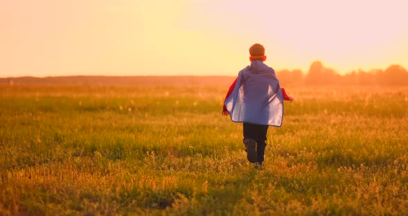 A Boy in a Superhero Costume at Sunset Runs Across the Field Laughing and Smiling