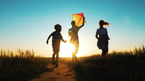 Happy Young Mother with a Children Play Kites Together on Park