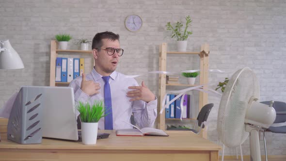 Young Man Working on a Laptop in the Office Sitting in Front of the Fan