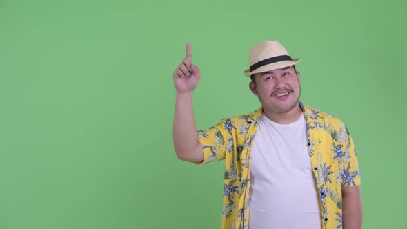 Happy Young Overweight Asian Tourist Man Talking While Pointing Up