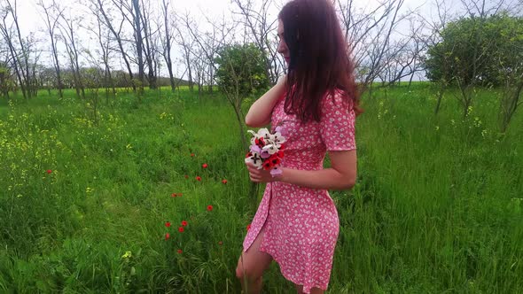 A beautiful woman in a floral dress holds a bouquet of wildflowers poppies in her hands