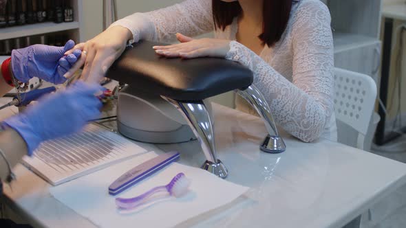 Unrecognizable Person in Gloves Saws Nails of Young Woman in Salon