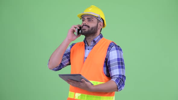Happy Overweight Bearded Indian Man Construction Worker Working While Using Phone and Digital Tablet