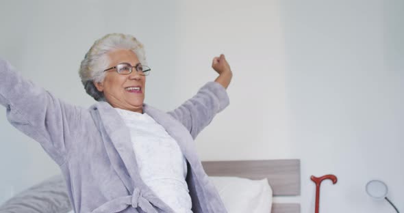 African american senior woman stretching her arms while sitting on the bed at home