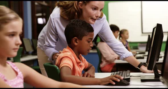 Teacher assisting school kids on personal computer in classroom