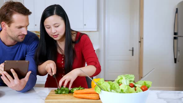 Couple using digital tablet while cutting vegetable in kitchen 4k