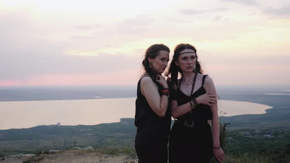 Two Girls in Black Dresses Stand on the Mountain in Summer