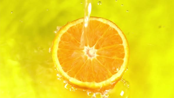 Water pours on an orange juicy orange on a yellow background slow motion closeup. Orange slice