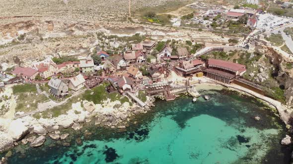 Establishing aerial shot of turquoise sea on a Mediterranean shore, Anchor Bay - Popyeye Village