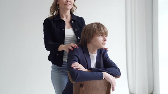 A Mother with Son in Blue Clothes Poses on a Chair By Window for a Photo Shoot