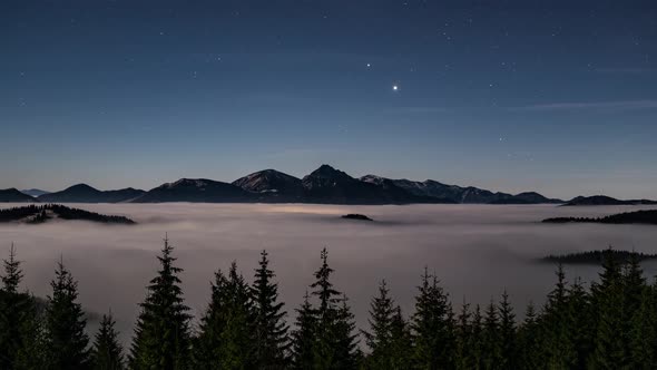 Blue Nigh Sky with Stars Above Alpine Mountains, Forest and Foggy Clouds in Evening Nature Lanscape