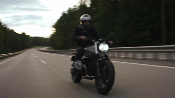 Man Riding Scrambler Motorbike on the Highway Through the Forest Front View