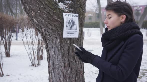 Side View of Smiling Caucasian Girl Calling on the Phone Number Written on Missing Dog Ad. Happy