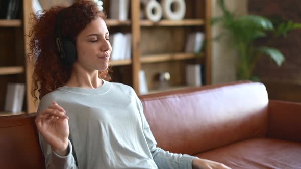 Joyful Curly Young Redhaired Woman Wearing Wireless Headphones Enjoying Listening Music