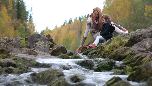A Young Mother and Her Cute Daughter Sitting Near the Forest Stream