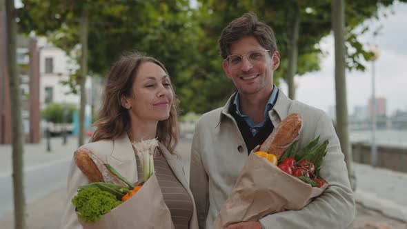 Couple Smiling on Camera and Holding Grocery Bags Outdoors