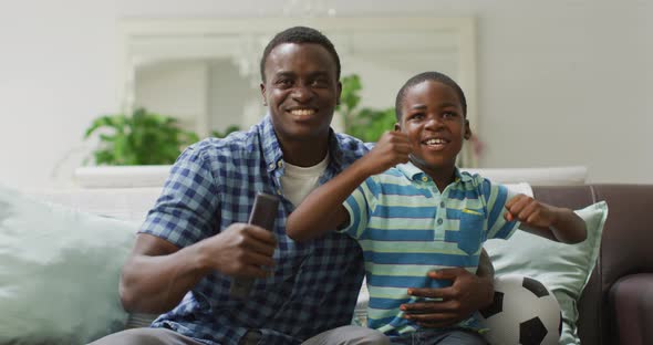 Happy african american father and son cheering while watching match in tv