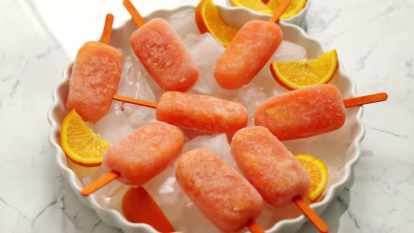 Homemade, Juicy, Orange Popsicles. Placed on a White Plate with Ice Cubes