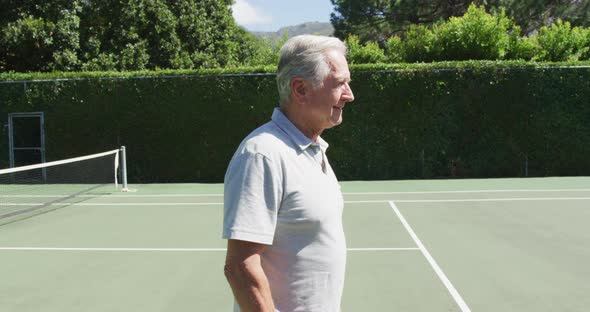 Portrait of caucasian senior man smiling while standing on the tennis court