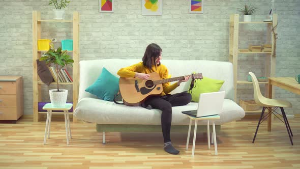 Young Woman Playing Guitar Learning on the Internet in Modern Apartments