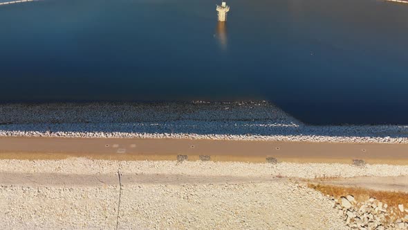 Aerial shot of a dam on a blue alpine lake surrounded by pine trees and mountains