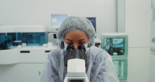 A Scientist in Sterile Clothing Looks Through a Microscope