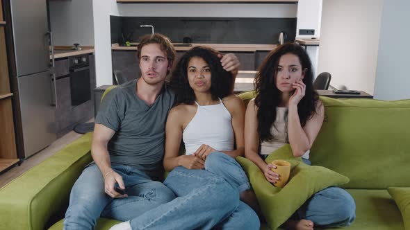 Group of Three Multiethnic Friends Watching Horror Movie on TV, Sitting on the Couch at Home. Young