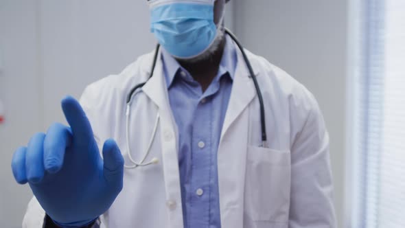 Midsection of african american male doctor wearing face mask and surgical gloves