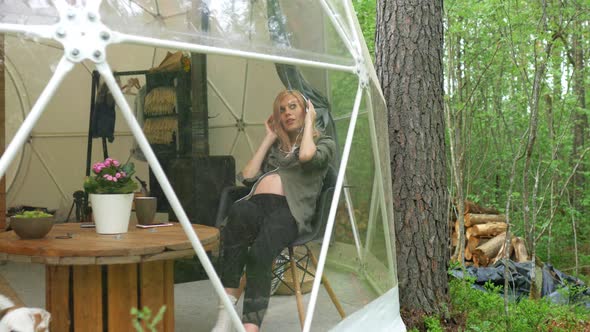 pregnant woman listens to music with headphones while sitting in a dome tent