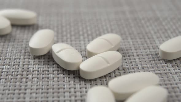 White oval pills fall on the textured plastic surface