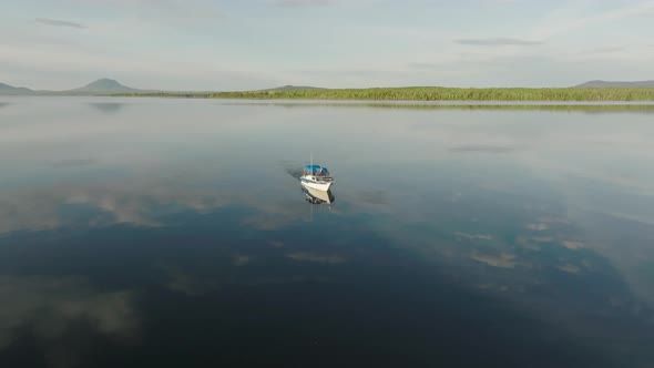 A boat alone crossing flat calm lake reflecting clouds