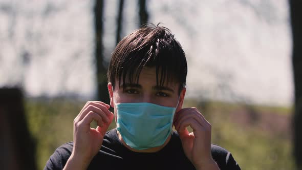 Close Up of Young Caucasian Man Taking on Medical Mask Outdoor. Sick Guy Wearing Protection During