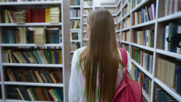 Student Walking Among Bookcases in Library