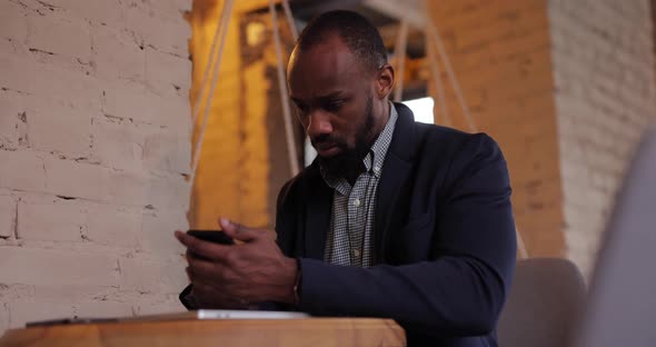 Serious African Businessman Using Smartphone Sitting in Cafe