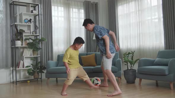 Happy Asian Father And His Son Playing Soccer In Living Room