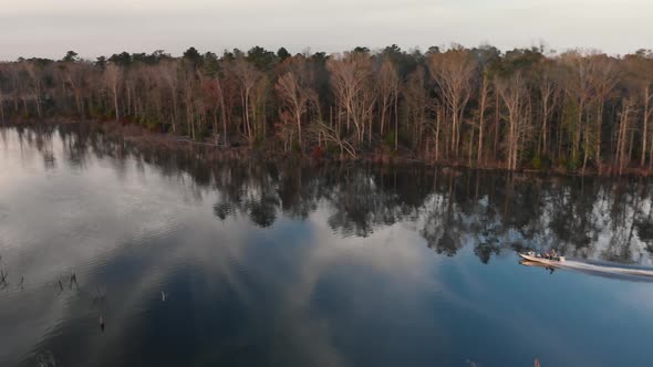 Following a single fishing boat as it speeds across the smooth surface of a lake in the golden eveni