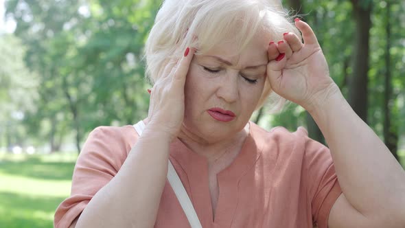 Close-up Portrait of Beautiful Senior Woman Having Headache and Migraine in Sunny Summer Park