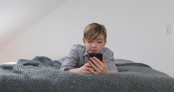 Boy using smartphone laying on bed at home