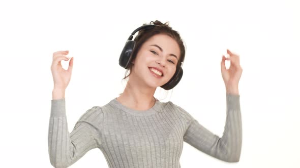 Joyful Smiling Caucasian Brunette Girl Dancing on White Background Listening Music Through Black