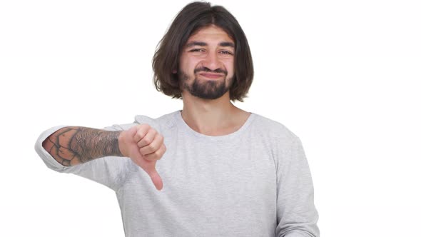Longhaired Caucasian Guy Gesturing His Thumb Down Isolated Over White Background