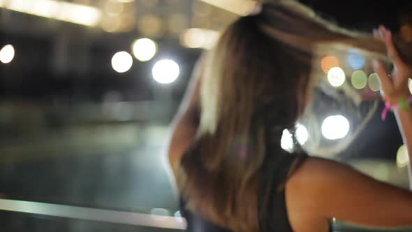 Teenage girl fixing hair absentmindedly while looking at view from pier at night