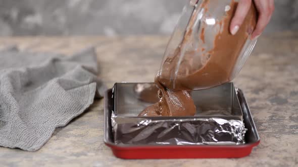 A Chef in the Kitchen Pouring Chocolate Cake Batter Into a Square Baking Pan To Go in the Oven 