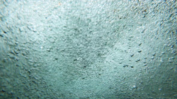 Bubbles rising underwater at base of small waterfall in a river