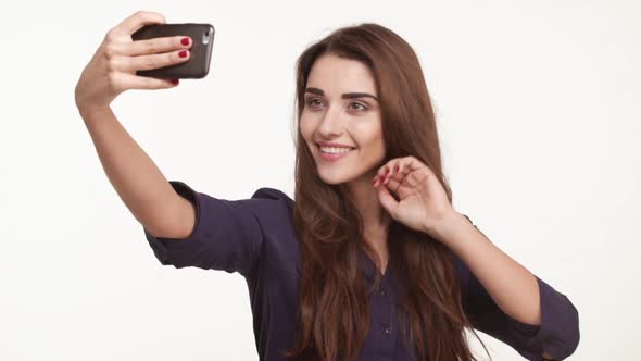 Beautiful Young Caucasian Female with Long Brown Hair Wearing Blue Shirt Making Selfie on Mobile