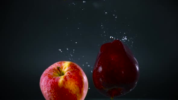 Red and Fuji apples falling into water slomotion.