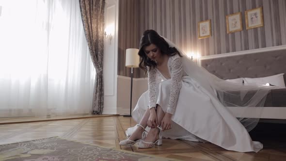 Young Bride in White Wedding Dress Wearing High Heeled Shoes on Slim Legs While Sitting at Home