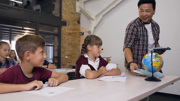 Teacher of Elementary School Walking Among Between Desks Puts Textbooks for Learning