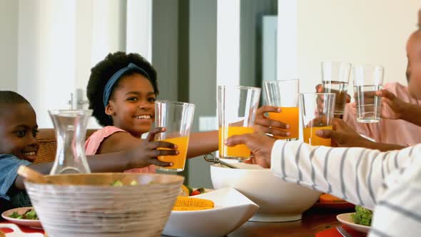 Side view of black multi generation family toasting glass of juice and water at dining table 4k