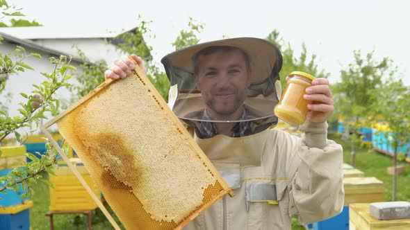 Beekeeper Holding a Honeycomb Frame and Jar with Honey